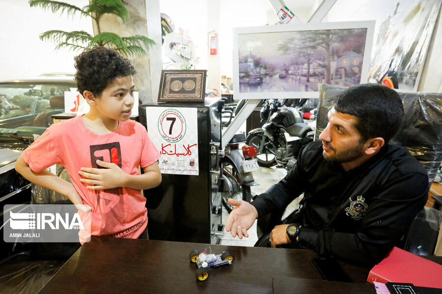 فرزند یکی از همسايگان نمایشگاه اتومبیل بهلول حسینی در نمایشگاه ماشین وی در حال نمایش خودروی کاردستی ساخت خویش.