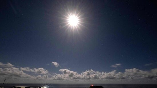 این عکس که با نوردهی طولانی گرفته شده است، ماه کامل را در آسمان ابری ساحل کیاما سرف نشان می‌دهد.
