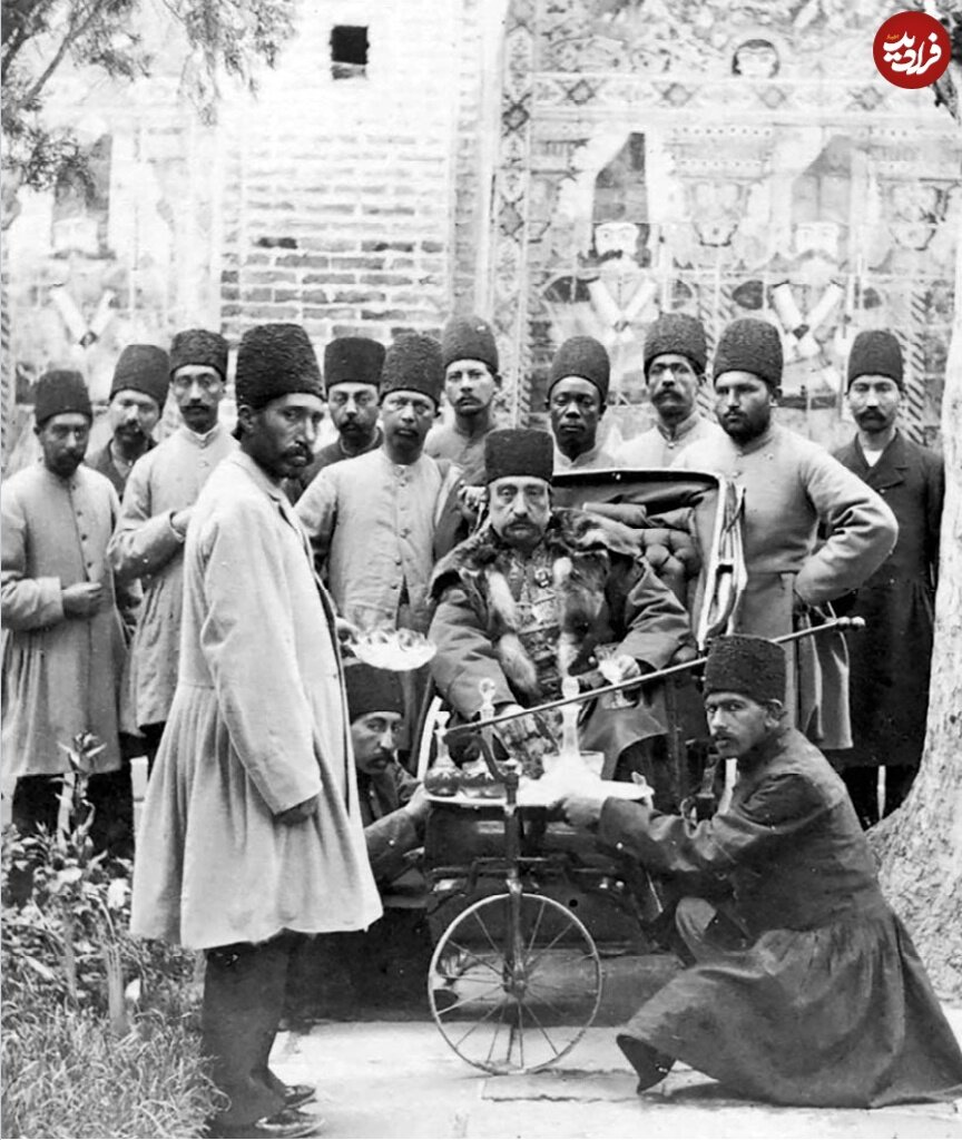ناصرالدین شاه سوار بر یک کالسکۀ سه‌چرخه در میان درباریان