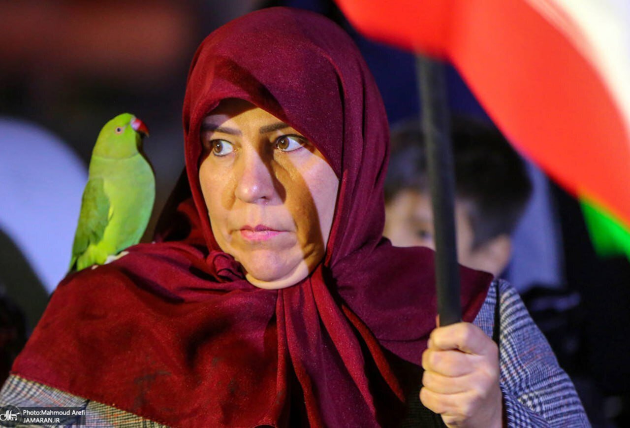 تصویری جالب از حضور یک زن در تجمع شبانه تهران با طوطی سبز و پرچم ایران